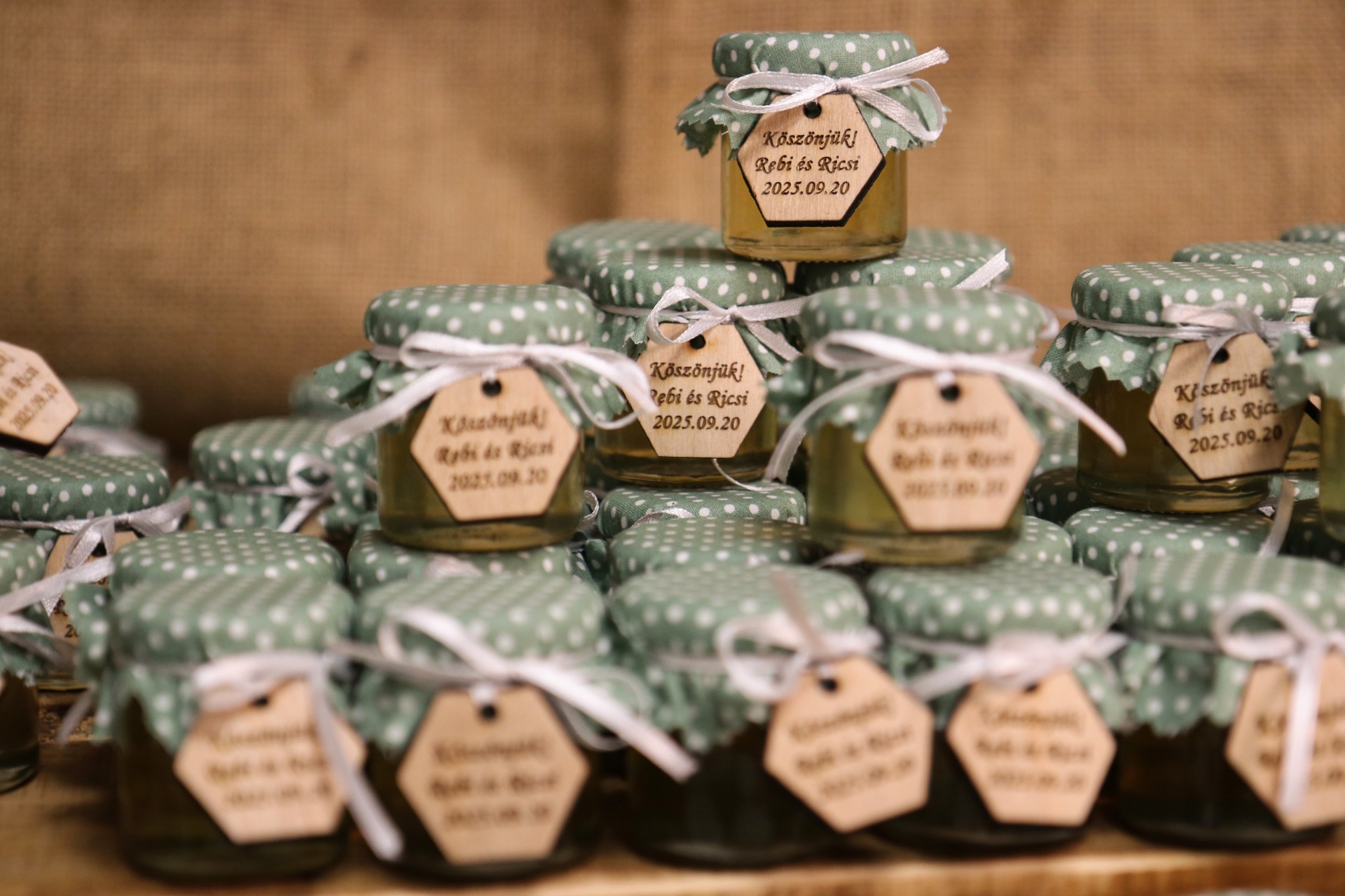 120db 50g-os akác méz esküvői köszönőajándék pöttyös anyagtetővel, fehér szaténszalaggal átkötve, egyedi fa lapocskán égetett felirattal.